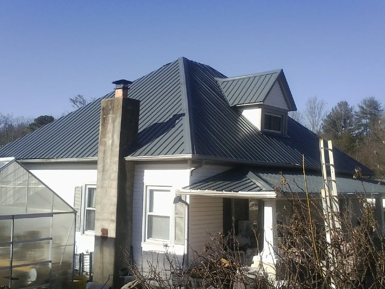 Dark blue standing seam metal roof on a white farmhouse with dormer — Slate & Tile Roof Repair by Roofing Brothers in Murdock