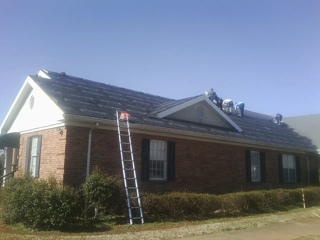 Crew tearing shingles off a brick ranch roof with a ladder set — Metal Roof Repair work by our crew in Murdock