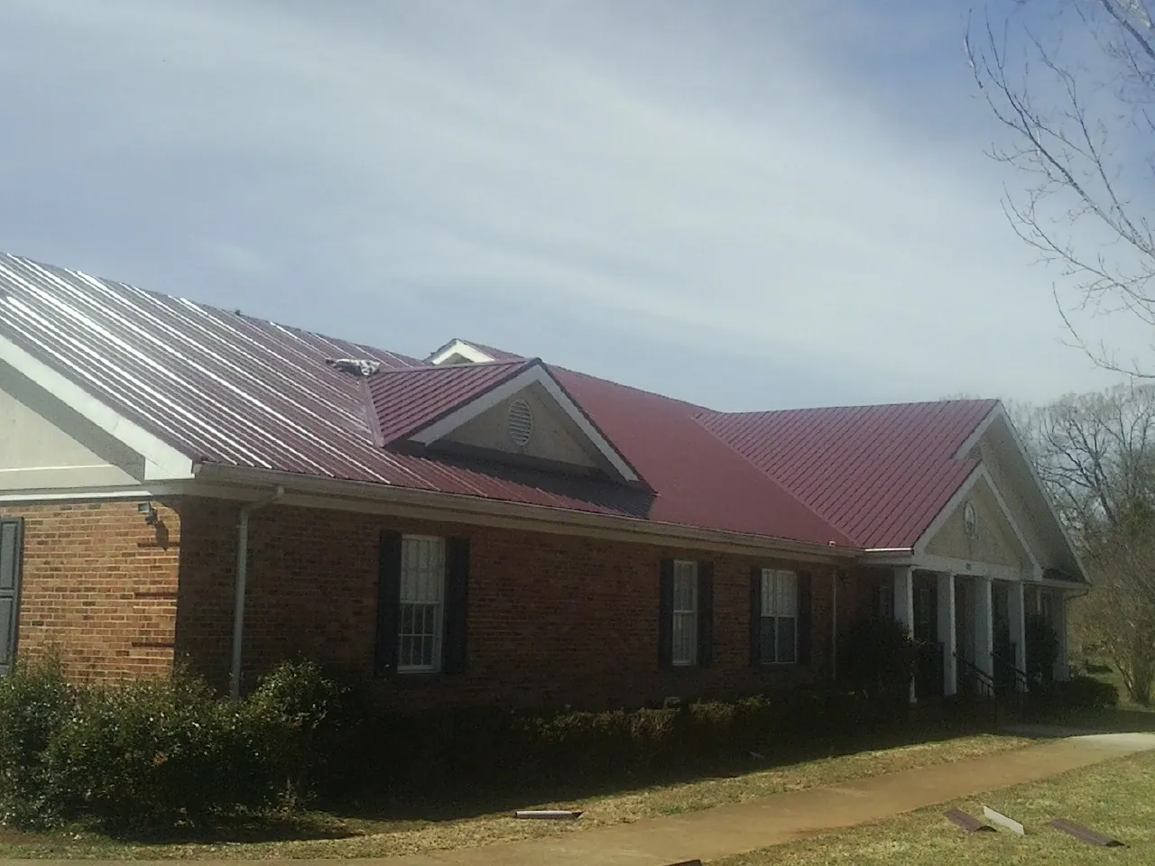 Red metal roof with gabled entries on a long brick building, from a Hail Damage Roof Repair job in Murdock
