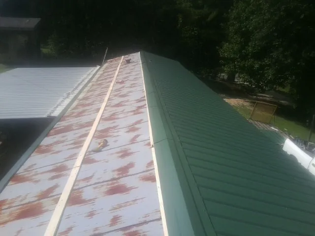 Old rusted panels beside newly installed green metal roofing — Wind Damage Roof Repair by Roofing Brothers in Murdock