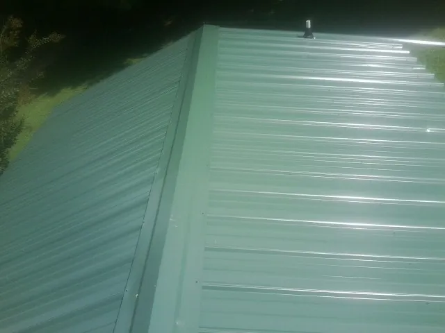 New green metal panels meeting at the ridge of a roof — Flat Roof Repair work by our crew in Murdock