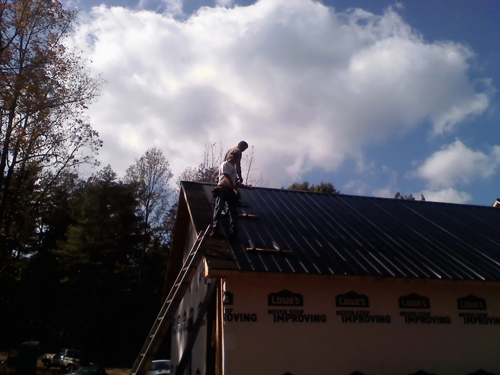 Roofer fastening dark metal panels high against a cloudy sky, from a Roof Inspection job in Murdock